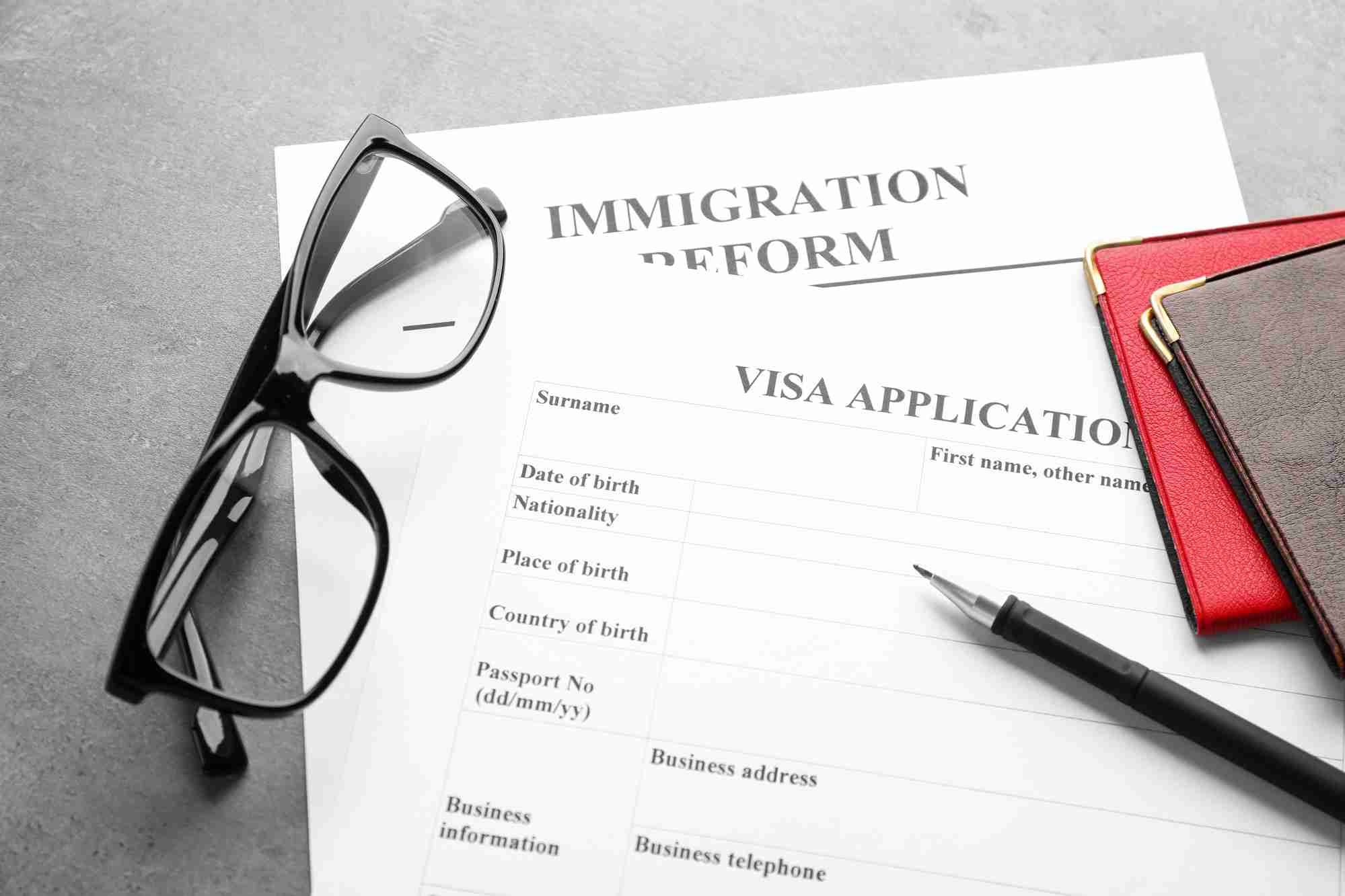 Passports, glasses and visa application form on table. Immigration reform